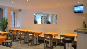 Un restaurante con mesas y sillas, un televisor en la pared y un ventanal con vista a edificios.