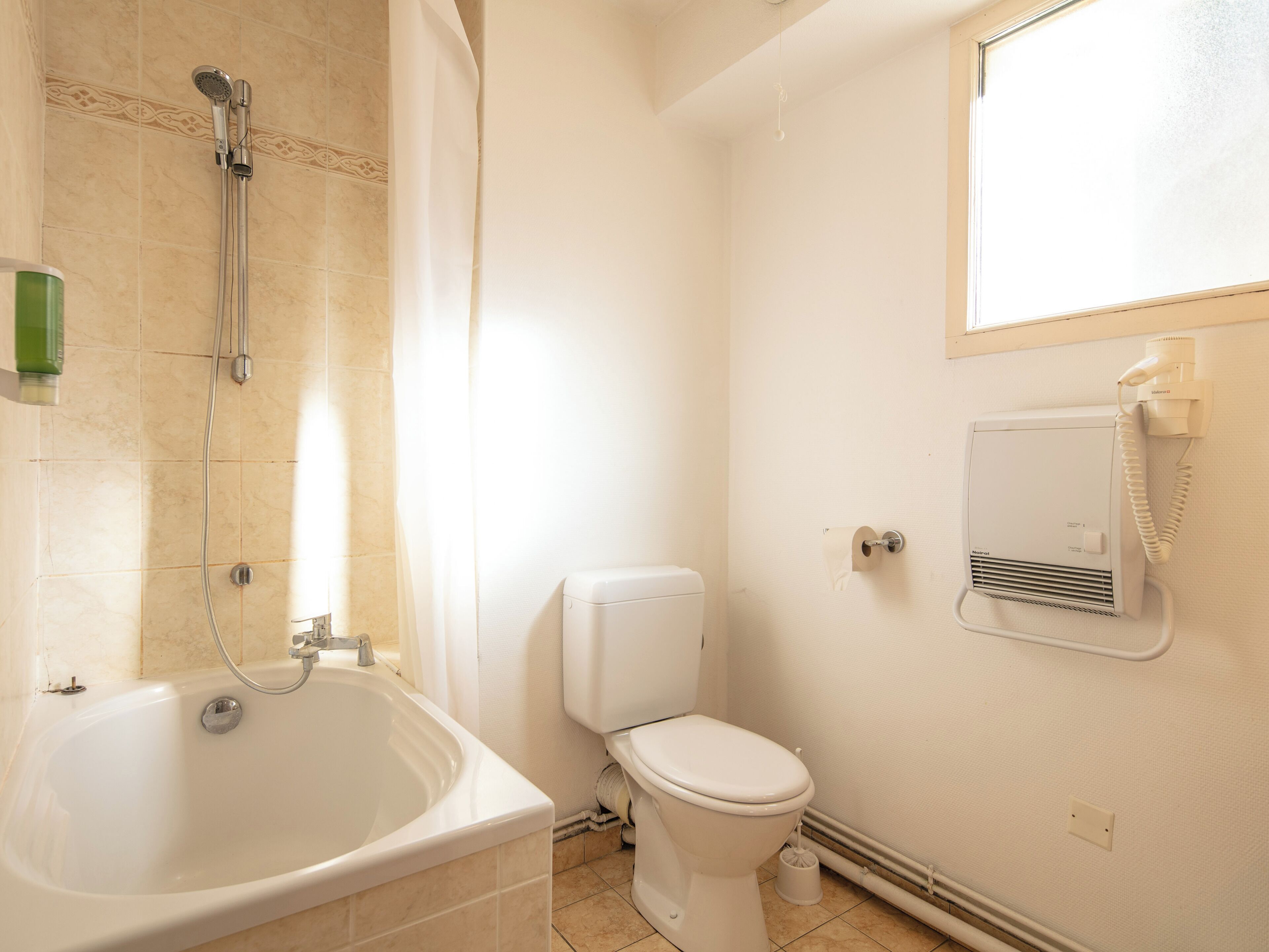 Un baño con bañera, inodoro y un calentador instalado en la pared.