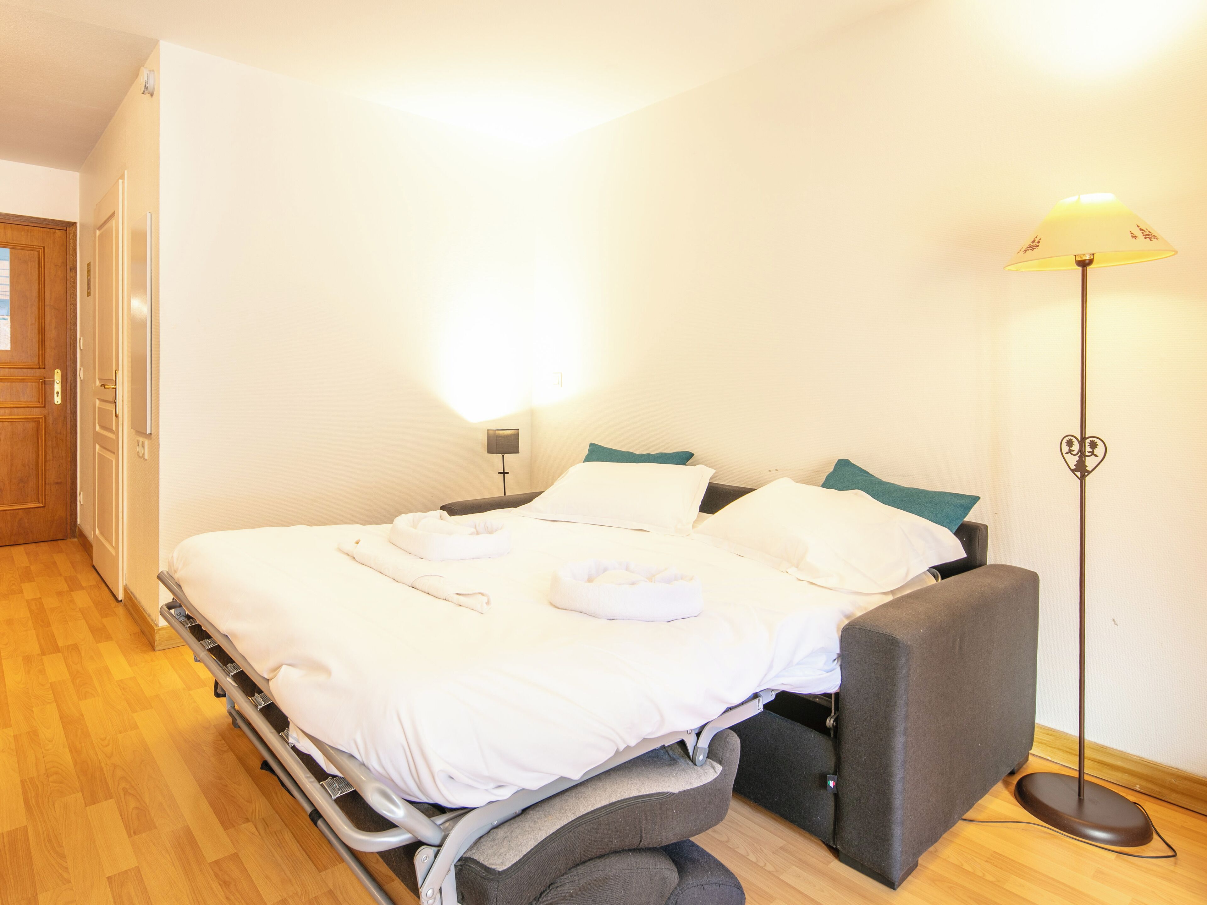 A bed with a headboard, a bedside table, a lamp, and a wooden floor.