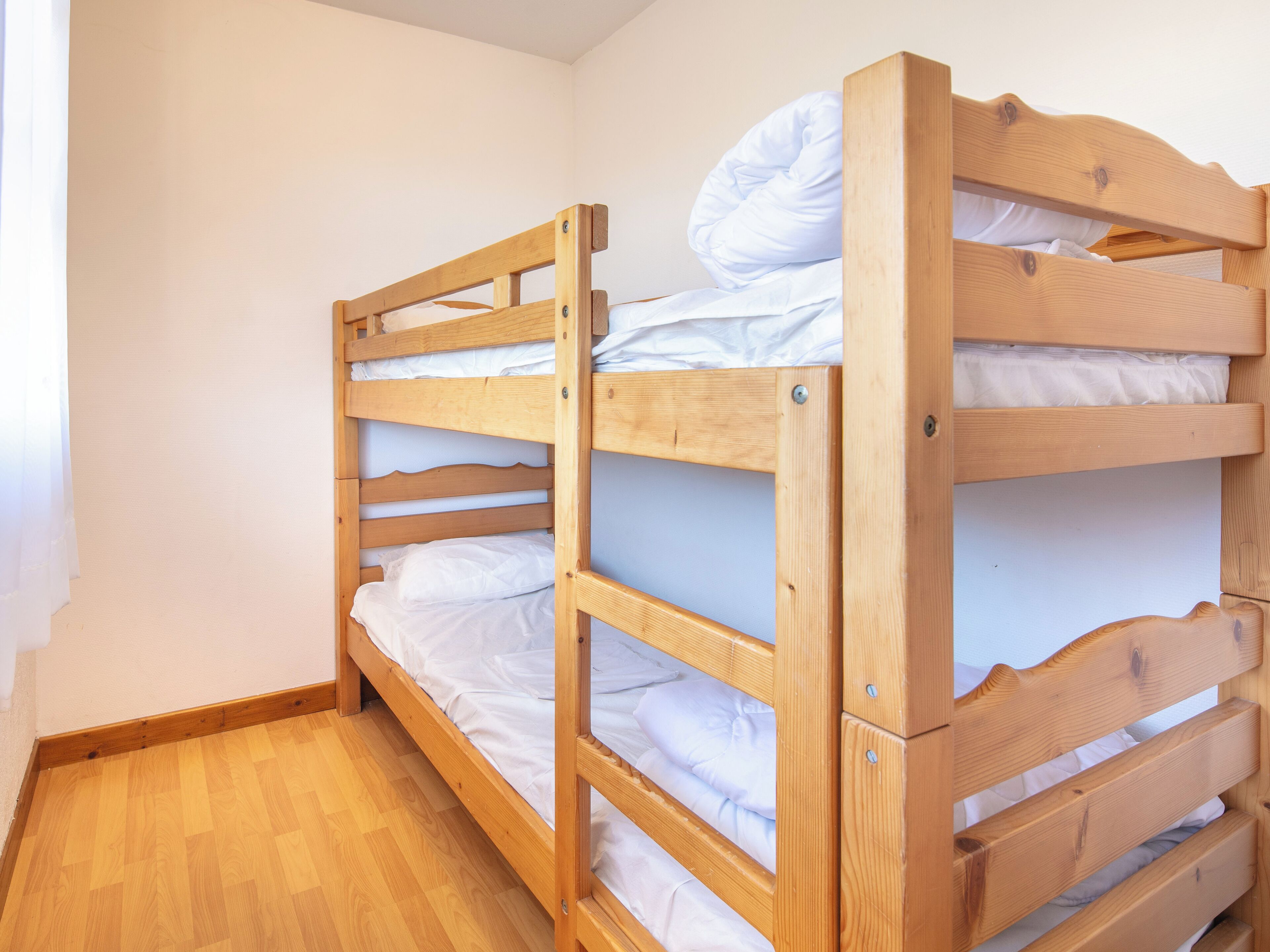 A bunk bed with white bedding in a room with wooden flooring and white walls.