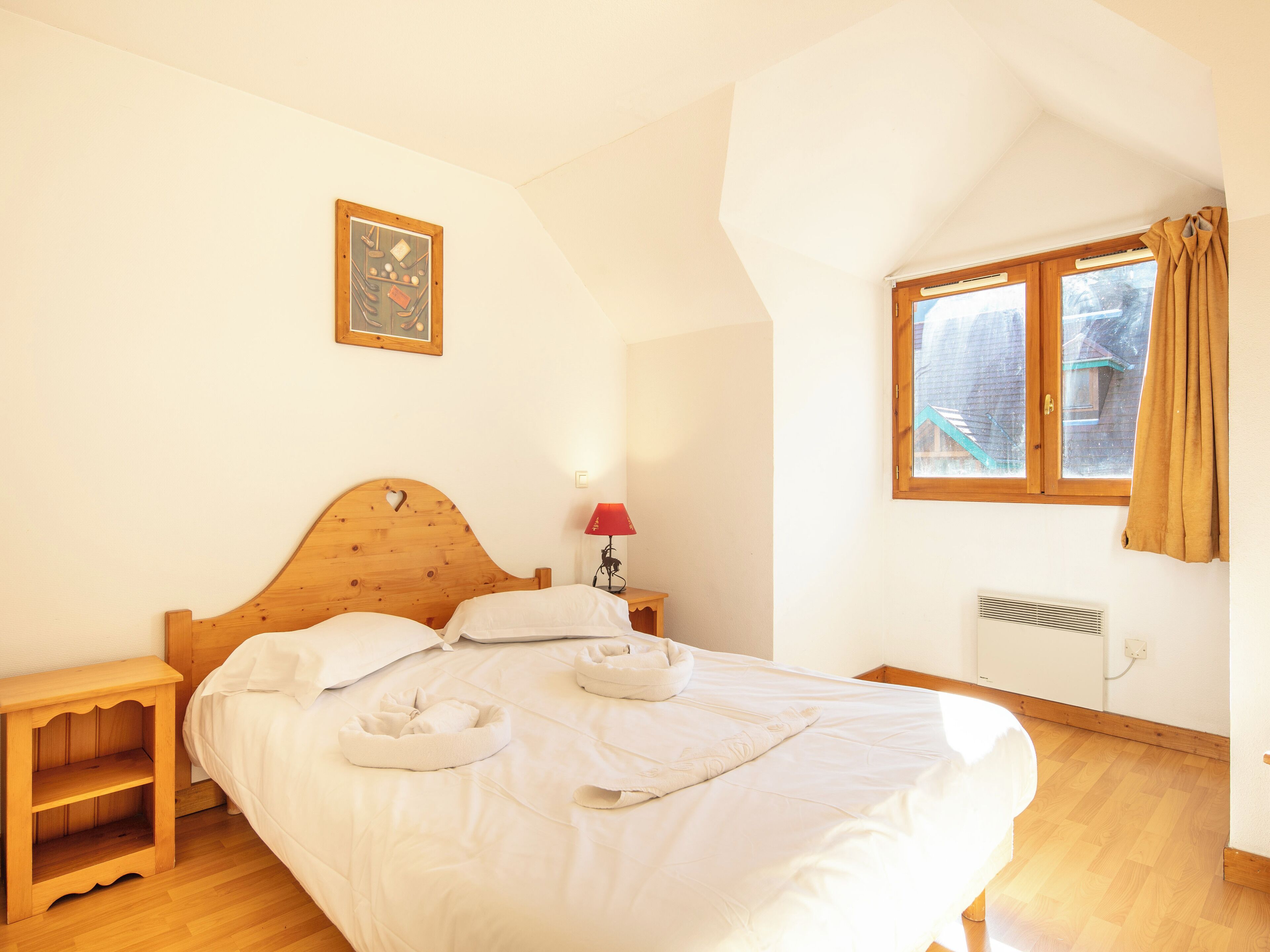 Une chambre à coucher avec un lit en bois, une table de chevet, une lampe, une fenêtre avec des rideaux et un radiateur.