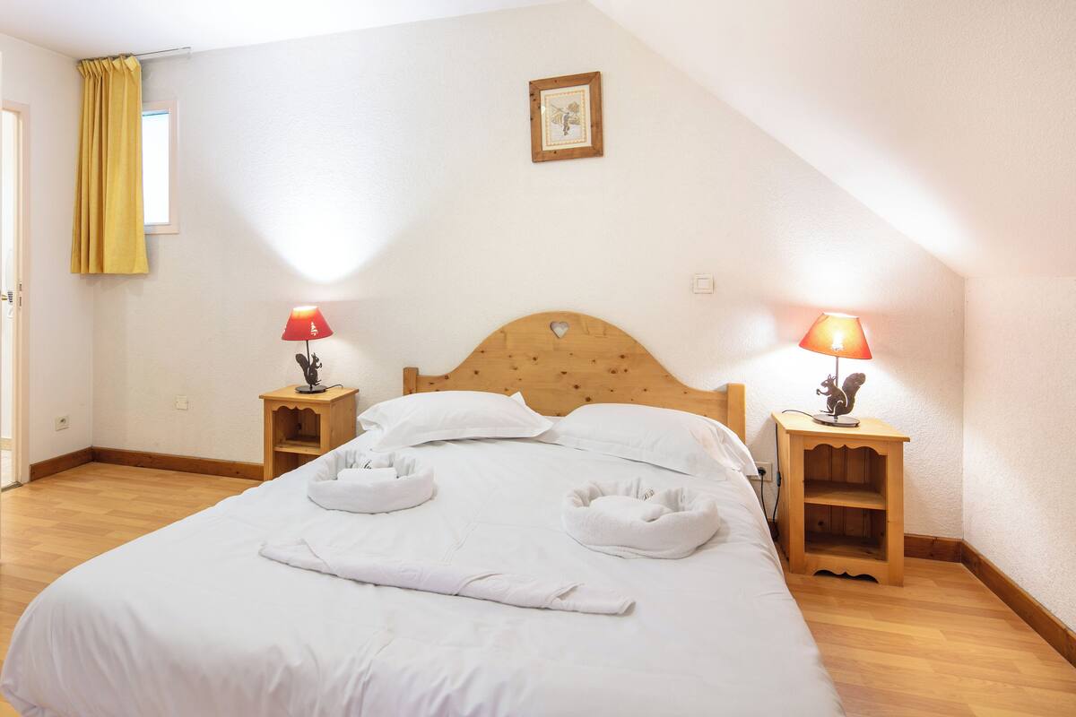 A neatly made bed with white linens and two bedside tables with lamps.