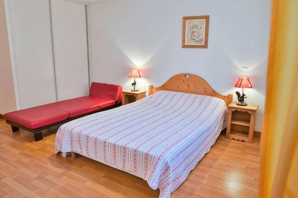 A single bed with a red mattress, a wooden headboard, two bedside tables with lamps, and a framed picture on the wall.