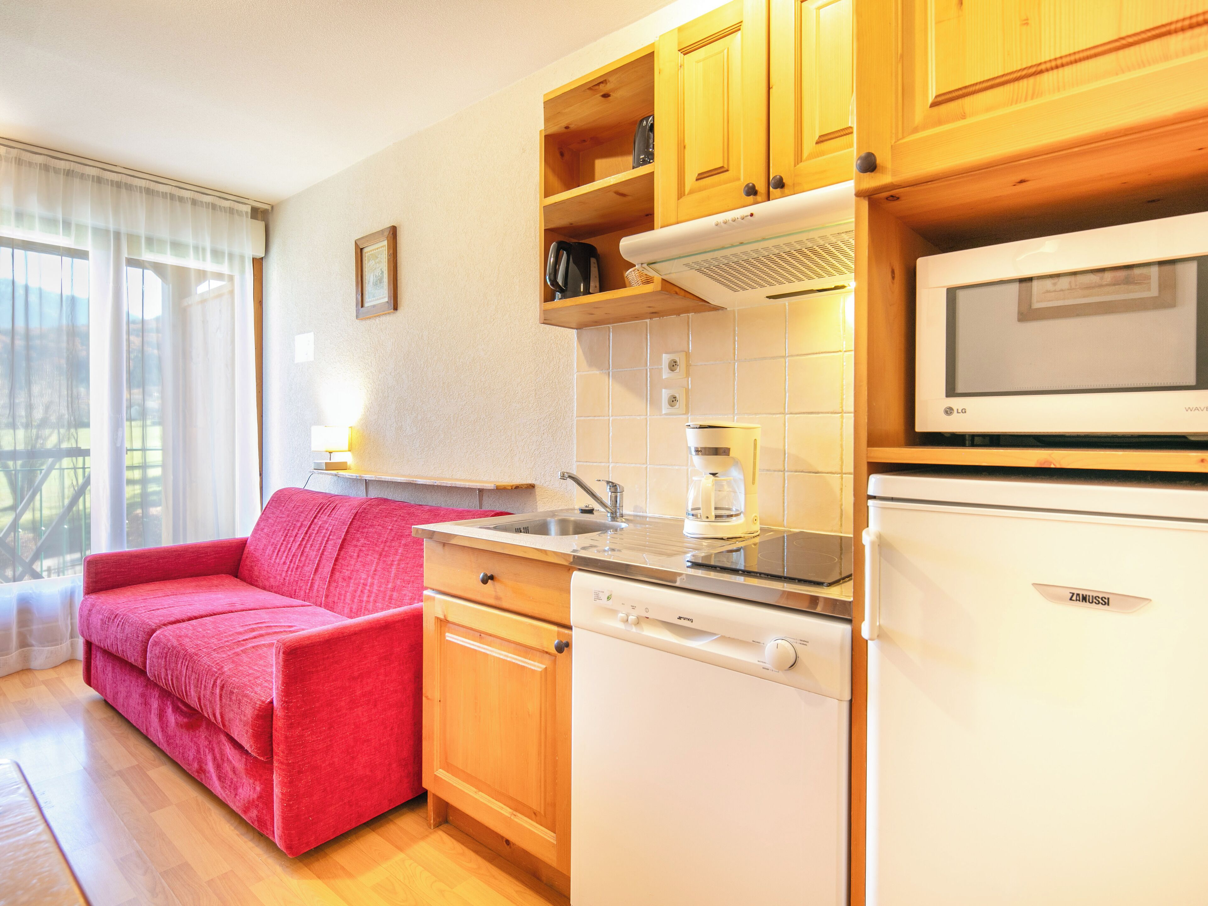 Una cocina compacta con armarios de madera, microondas integrado, cafetera y lavavajillas.