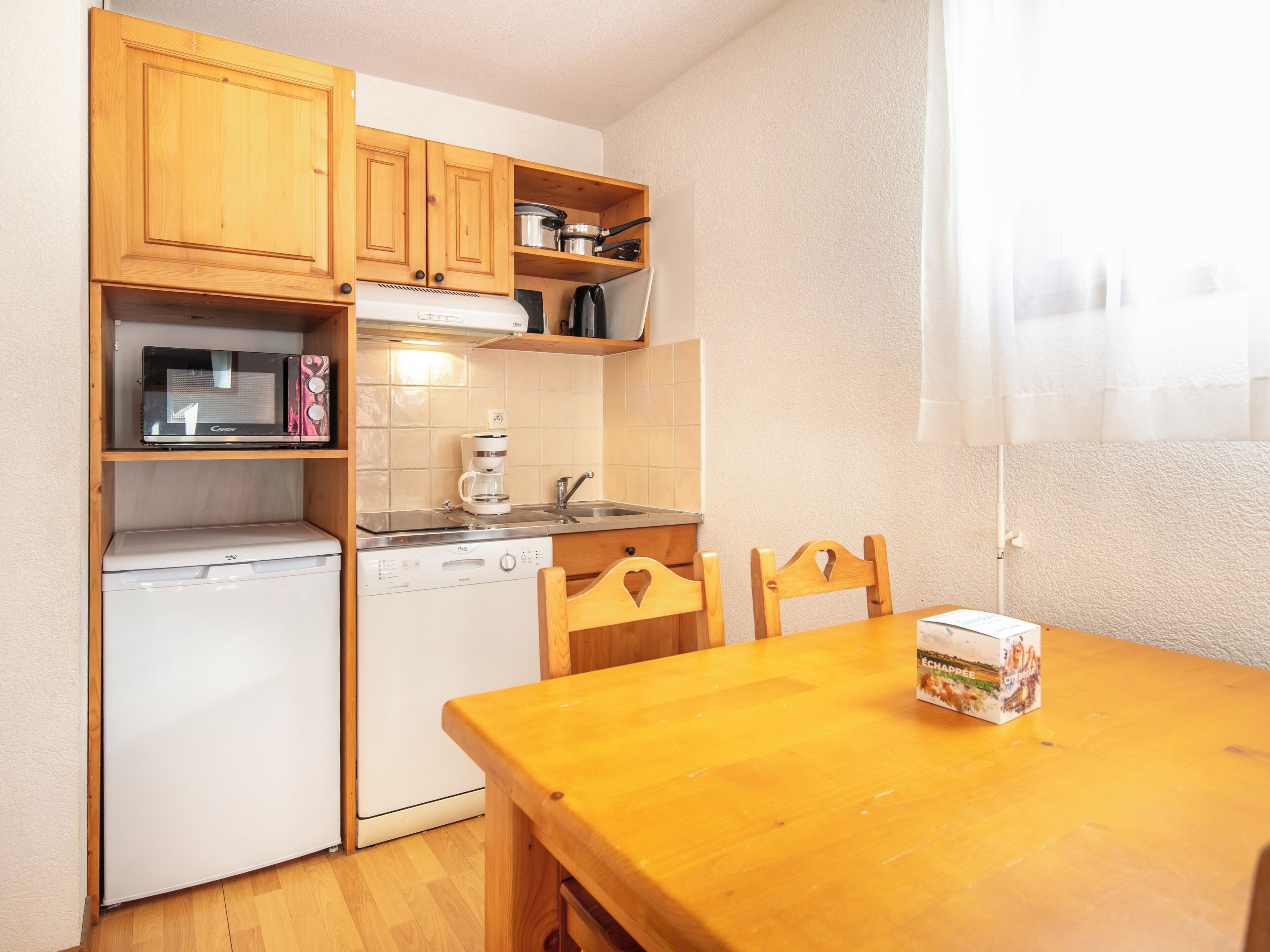 A compact kitchen with wooden cabinets, a microwave, a coffee maker, and a dishwasher.