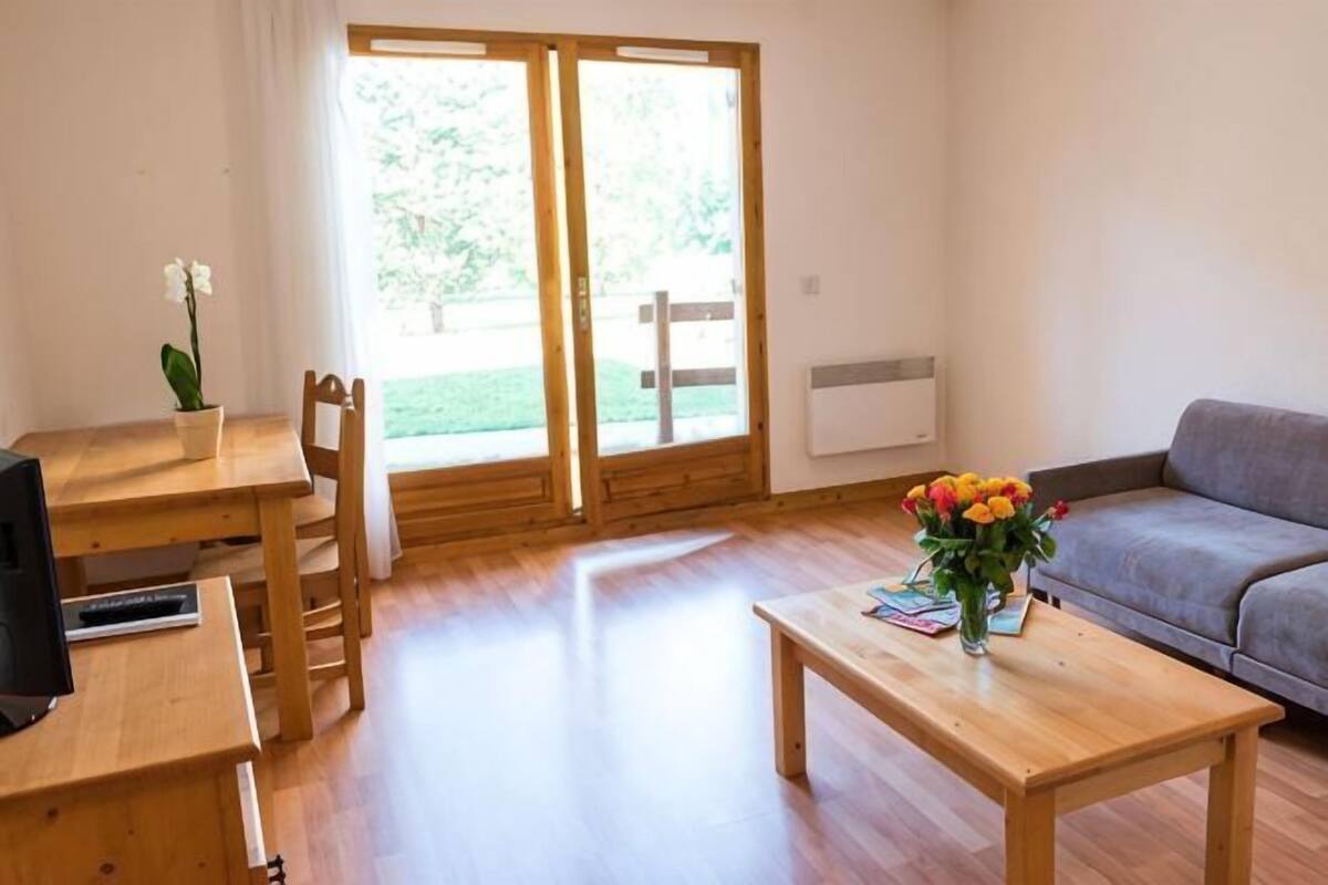 A room with a wooden table, a sofa, a TV, and a sliding glass door to the outside.