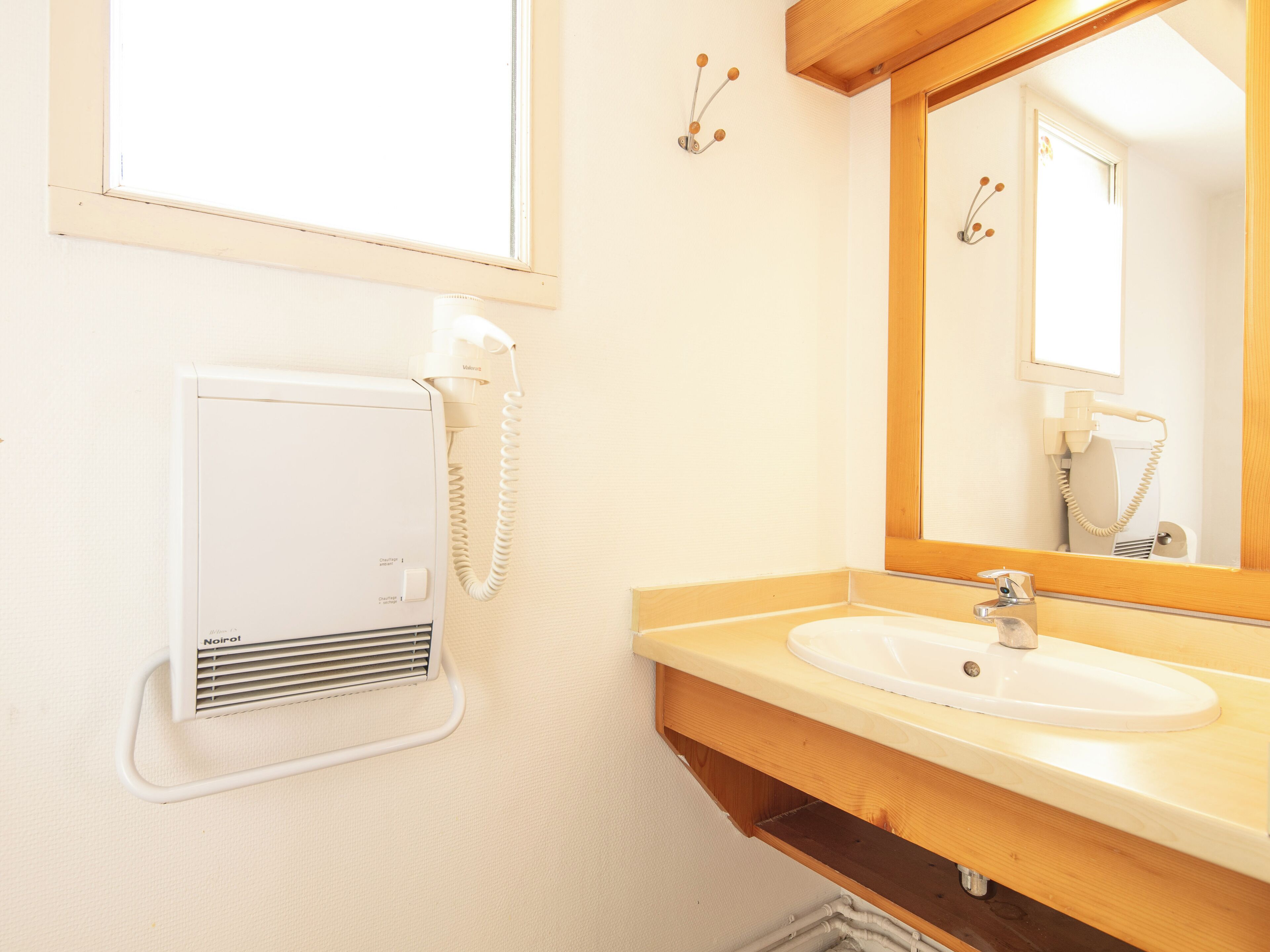 A bathroom with a white sink, wooden vanity, a mirror, and a hairdryer.