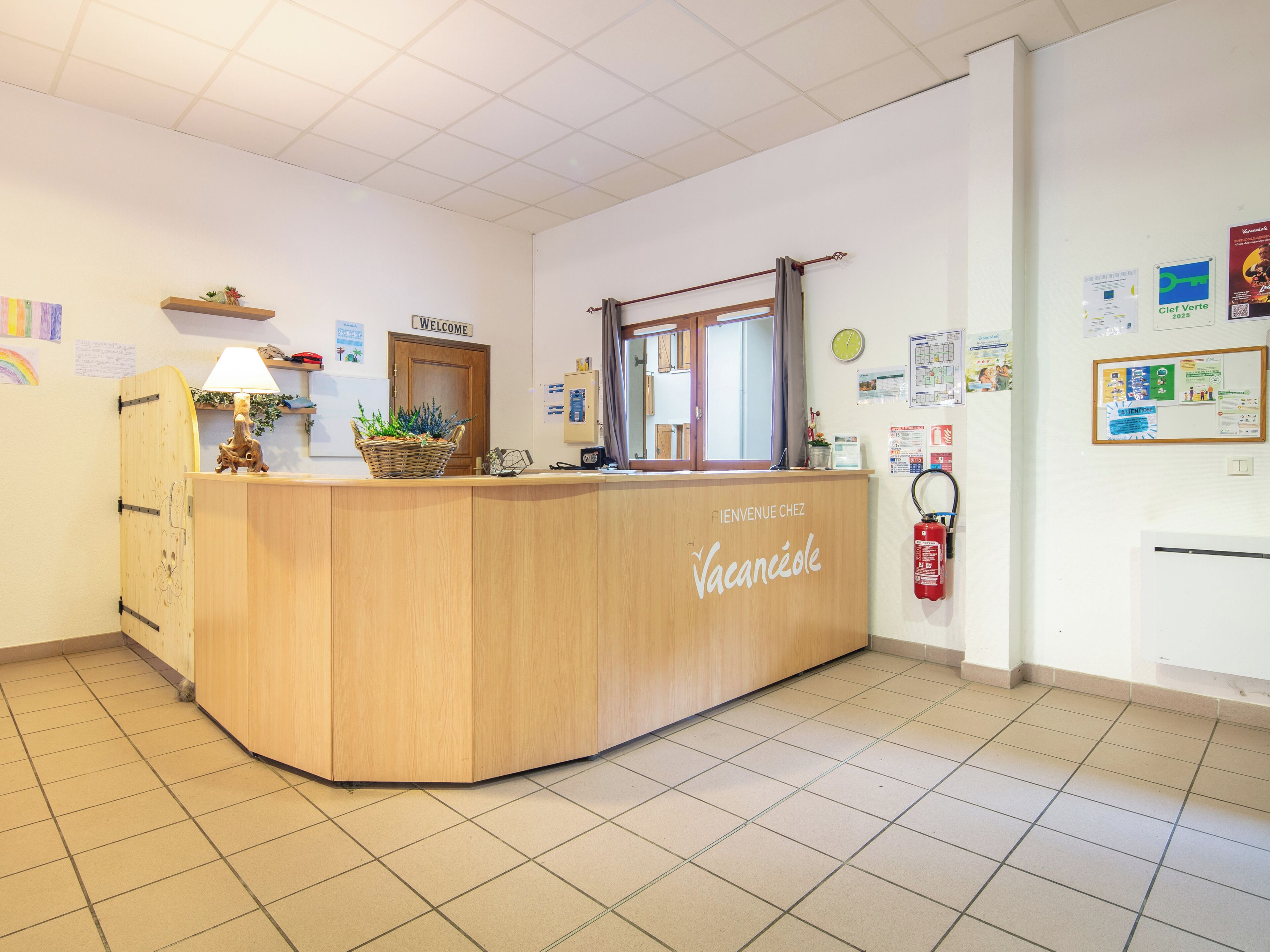 A reception desk with a "Welcome" sign, a clock, and various notices on the wall.