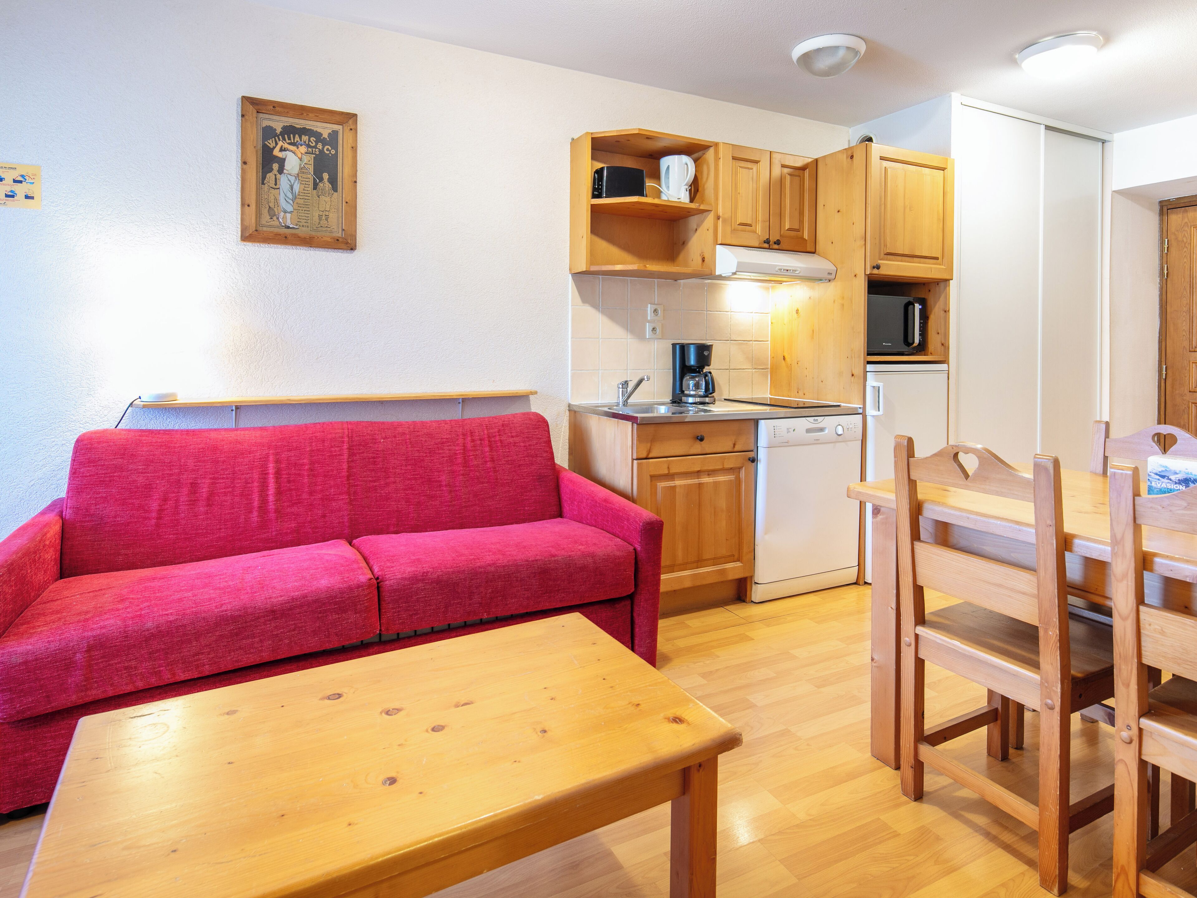 Eine kleine Küche mit Holzausstattung, einem roten Sofa und einem Esstisch.