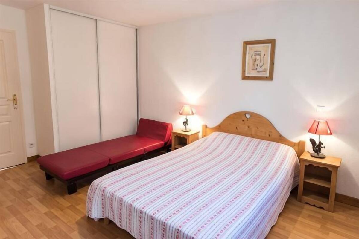 A single room with a bed, a red mattress, two bedside tables with lamps, a wooden headboard, and a framed picture on the wall.