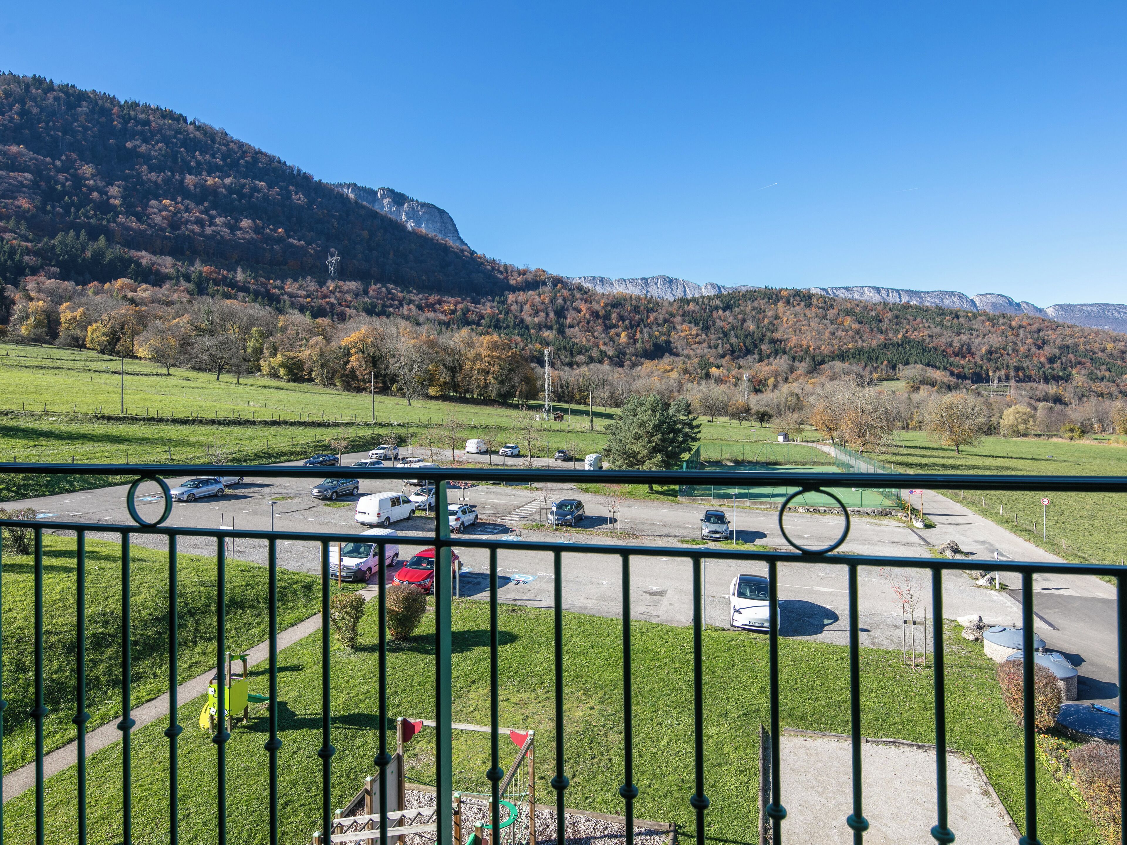 Un parking rempli de voitures, une aire de jeux et une montagne en arrière-plan.
