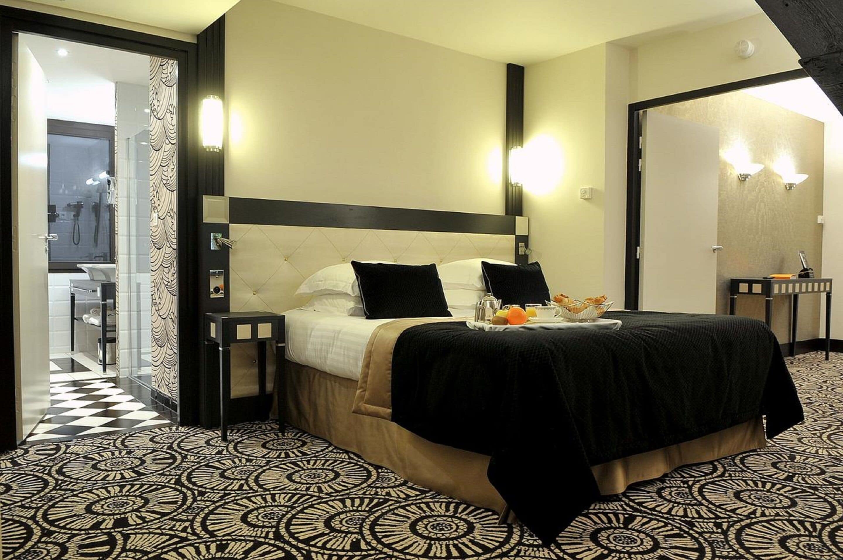 A hotel room with a bed, bedside tables, a bathroom visible through an open door, and a patterned floor.