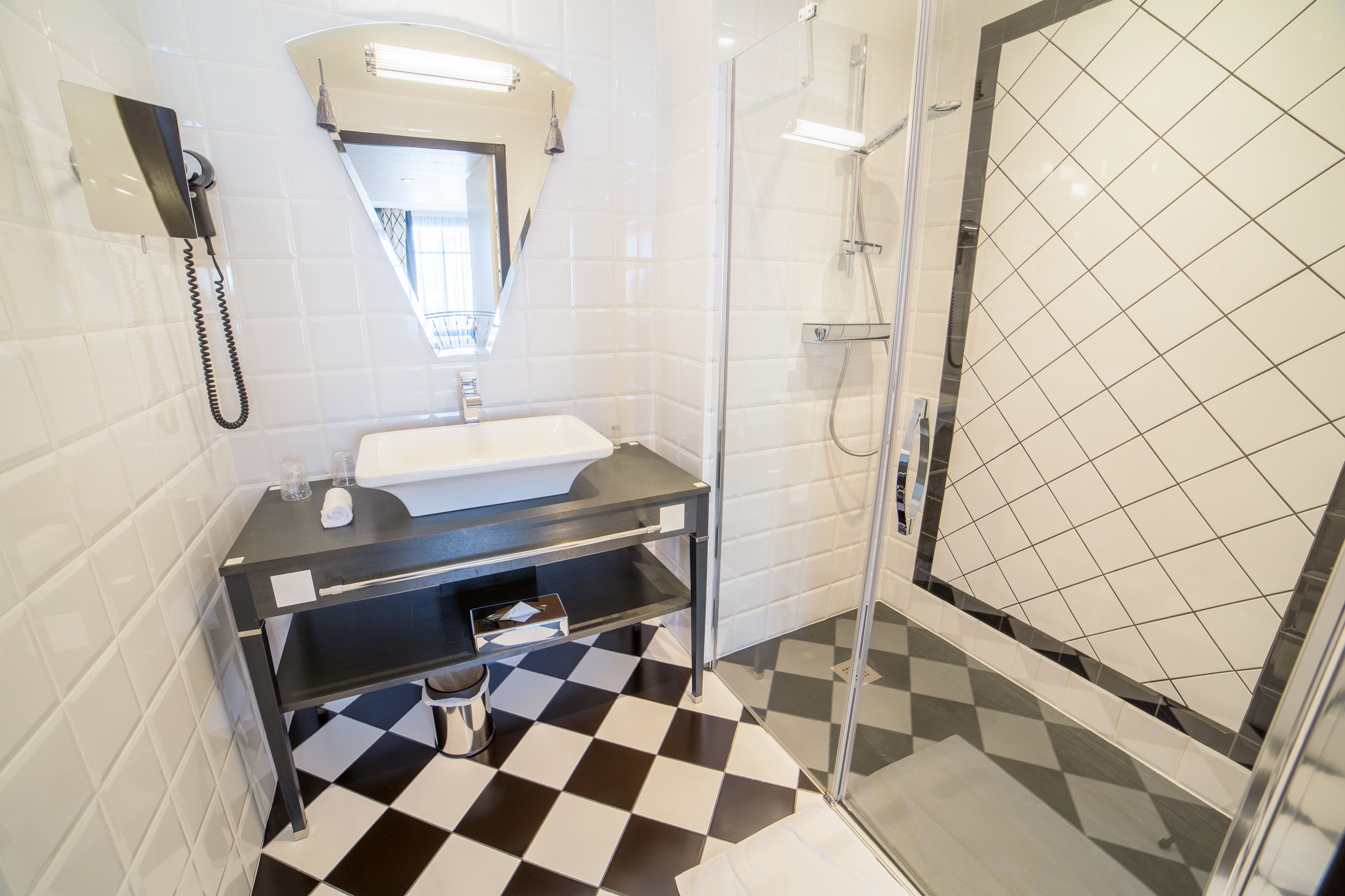 Une salle de bain avec un carrelage noir et blanc à motifs de damier, un lavabo, un miroir et une douche en verre.