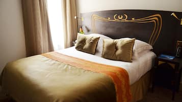 Un lit bien fait, recouvert d’une couvre-lit aux motifs dorés et blancs, agrémenté d’une tête de lit décorative et d’une table de chevet avec une lampe.