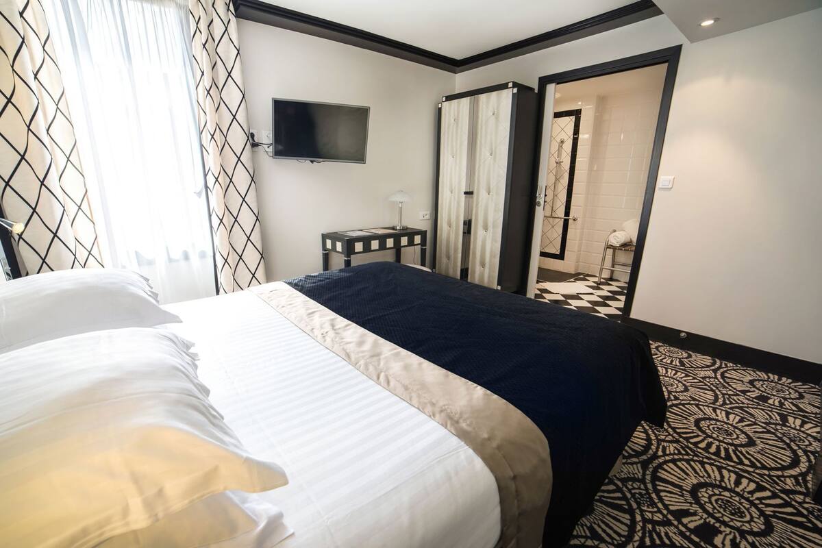 A hotel room with a bed, a TV mounted on the wall, a small table, and a mirror.