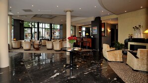 A spacious lobby with a marble floor, comfortable seating, and large windows offering a view of the outside. - Hotel Jehan de Beauce (Chartres)