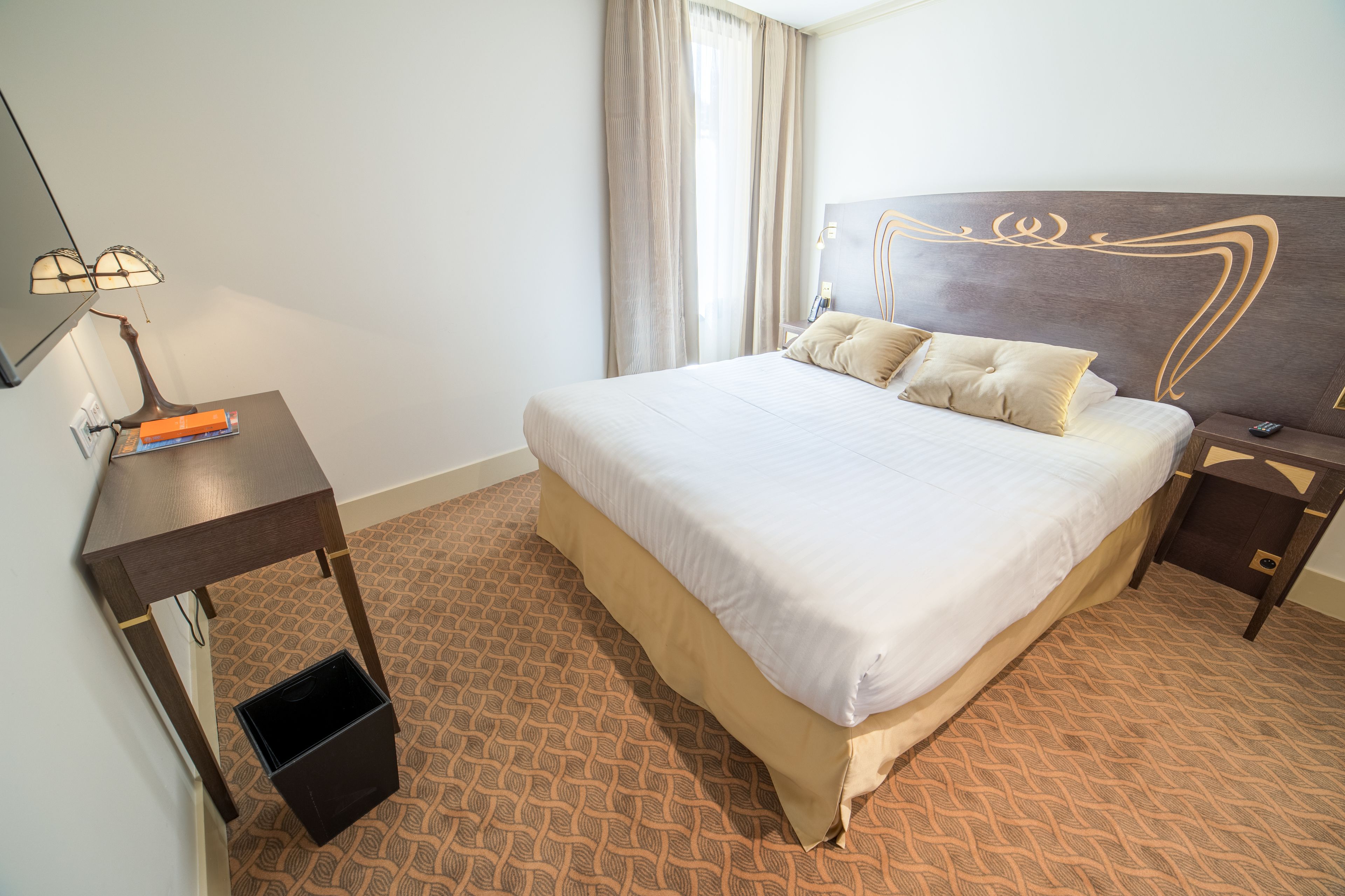 Habitación de hotel con una cama grande, un escritorio con lámpara y un pequeño cubo de basura.