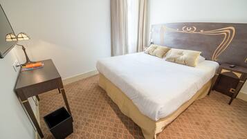 Habitación de hotel con una cama grande, un escritorio con lámpara y un pequeño cubo de basura.