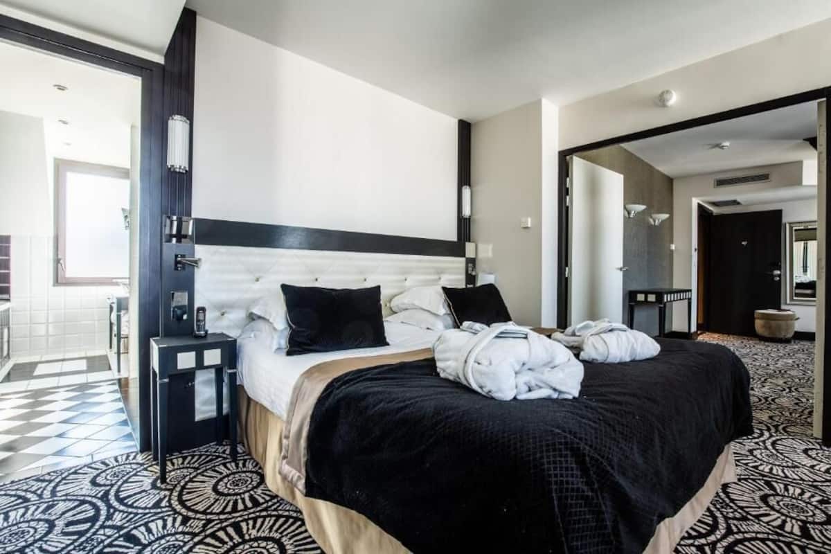A modern hotel room with a large bed, a bedside table, and a patterned floor.