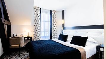 A hotel room with a large bed, a bedside table with a lamp, a chair, and a patterned carpet.