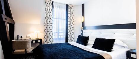 A hotel room with a large bed, a bedside table with a lamp, a chair, and a patterned carpet.