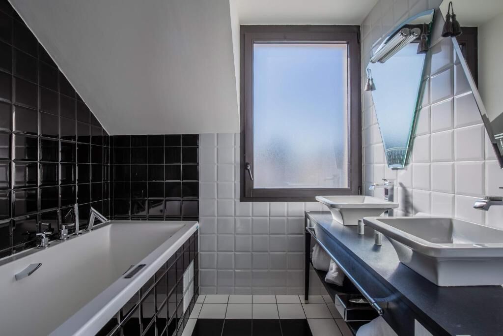 A modern bathroom with a large window, two sinks, a bathtub, and a mirror.