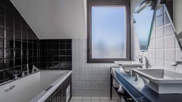 A modern bathroom with a large window, two sinks, a bathtub, and a mirror.