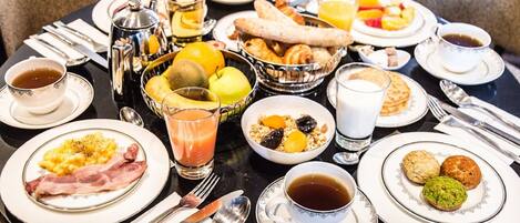 Un bufé de desayuno con diversos platos, como huevos, tocino, bollería y fruta.