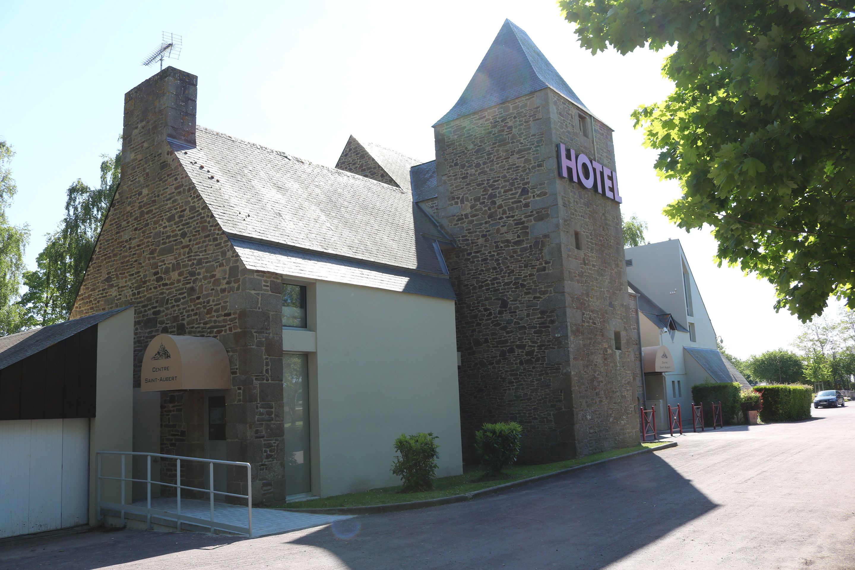 En byggnad av sten med en skylt som visar texten ”HOTEL”, en liten entré och en parkeringsplats.