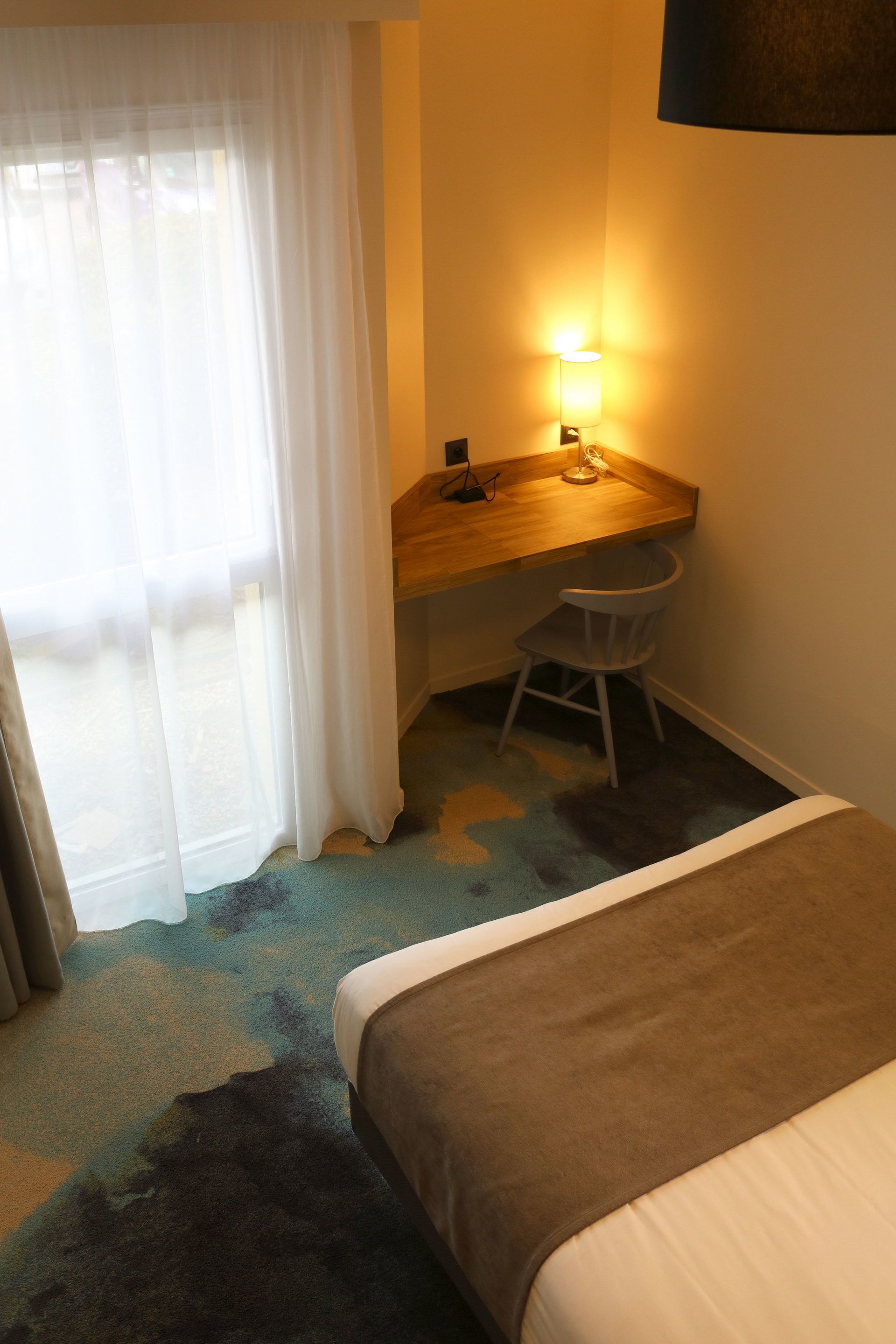 Una habitación de hotel con una cama, un escritorio, una silla y una lámpara.