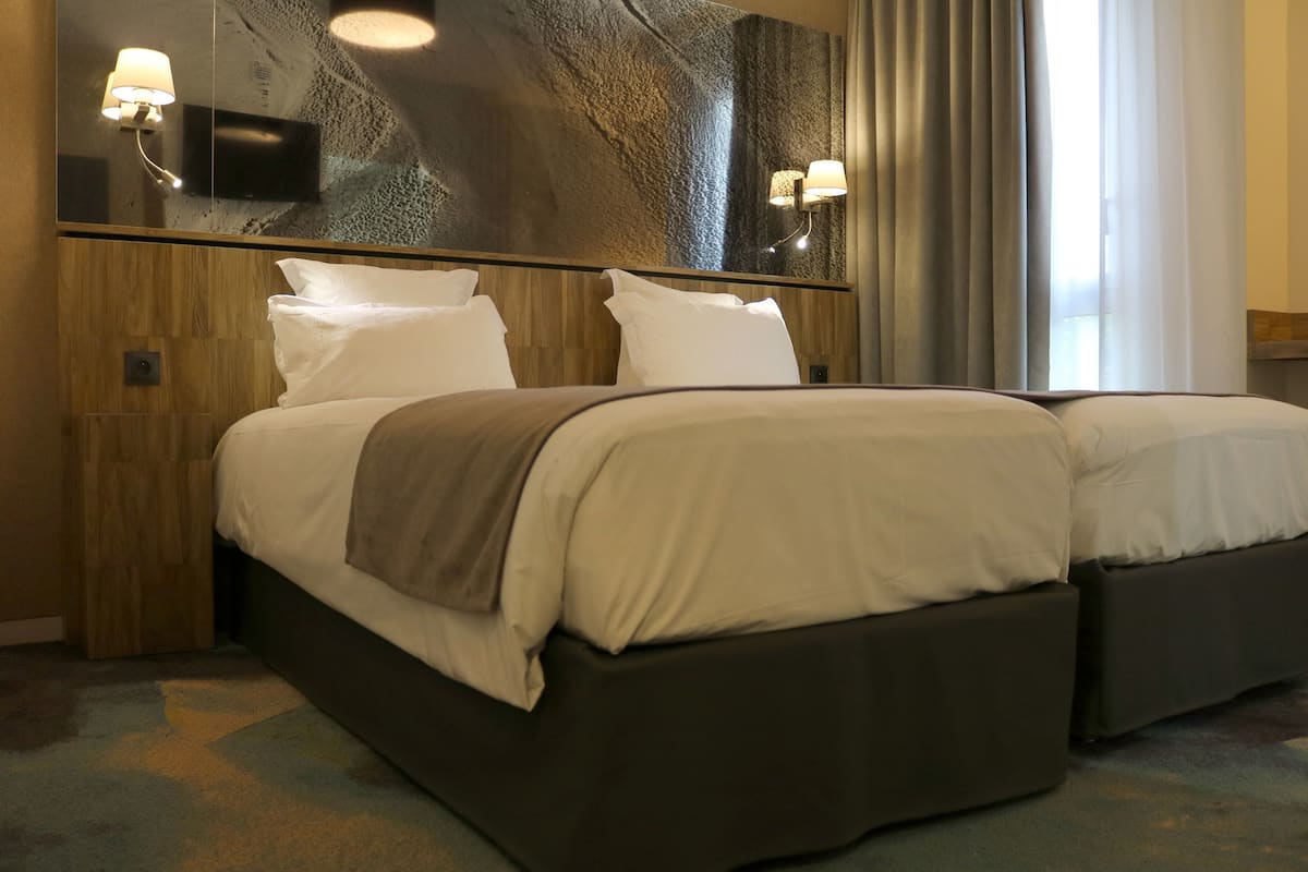 A hotel room with a large bed, a smaller bed, a mirror, and a wall-mounted TV.