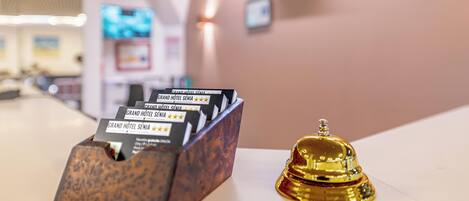 Un mostrador de recepción de madera con una campana y un porttarjetas que muestra información del hotel.