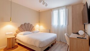 A bedroom with a bed, bedside table, desk, chair, and a TV. - Grand Hôtel Senia (Orly)