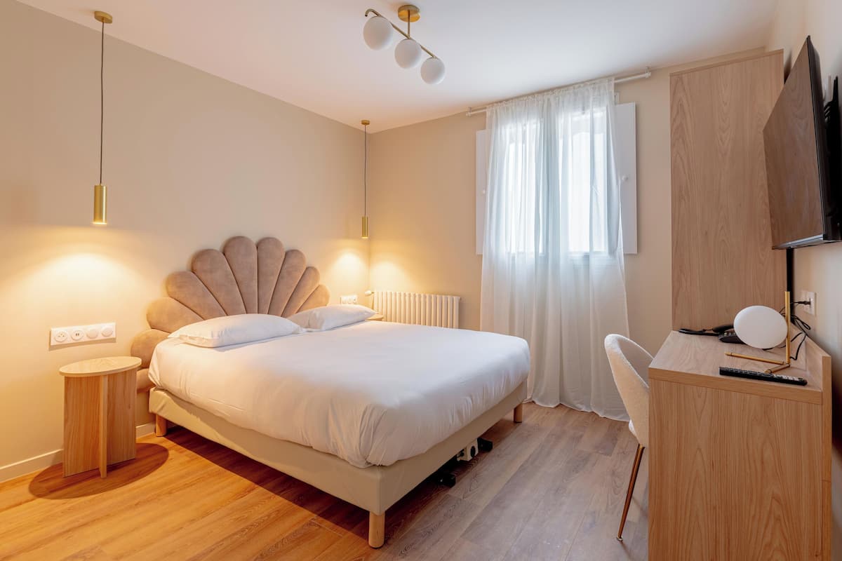 A bedroom with a bed, bedside table, desk, chair, and a TV.