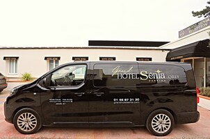 Una camioneta negra con la leyenda 'Grand Hotel Senia' y 'Orly Parking', estacionada frente a un hotel con varios letreros de 'Hotel Senia'.