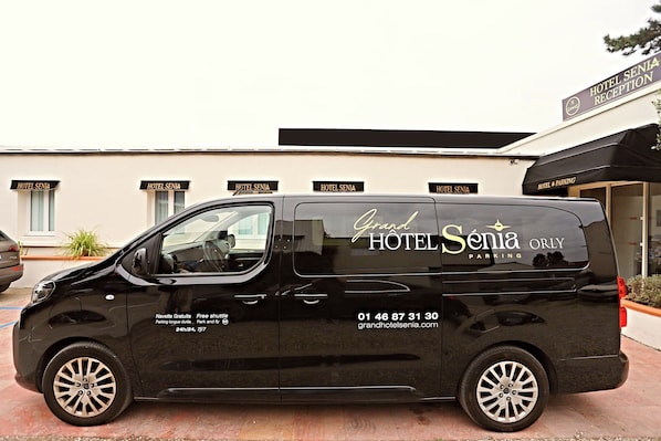 A black van with 'Grand Hotel Senia' and 'Orly Parking' written on it, parked in front of a hotel with multiple 'Hotel Senia' signs. - Grand Hôtel Senia (Orly)
