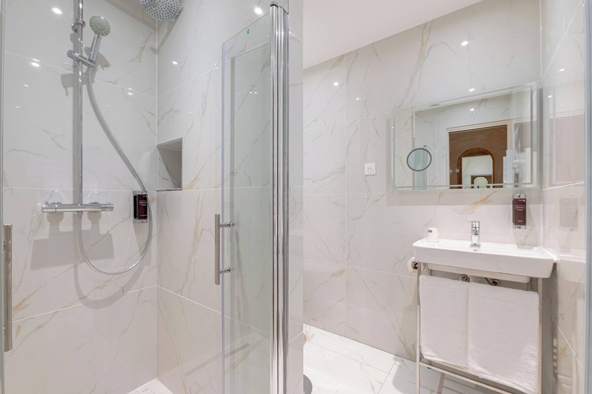 A modern bathroom with a glass-enclosed shower, a sink with a mirror, and marble-patterned walls.