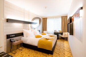 A hotel room with a large bed, a desk, a chair, a TV, and a phone on the side table.