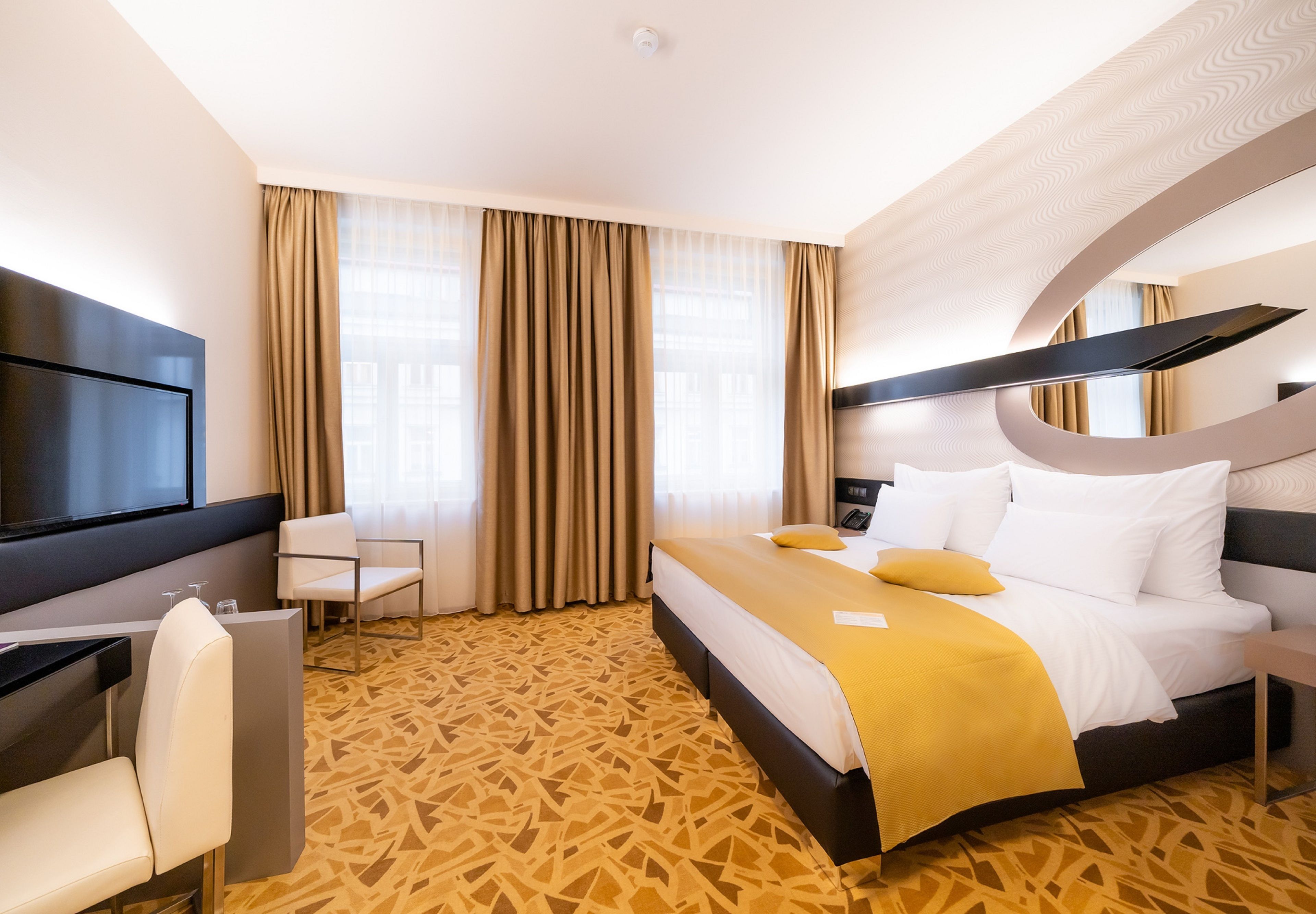 Habitación de hotel con cama, escritorio, silla, televisor y alfombra estampada.