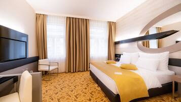 A hotel room with a bed, a desk, a chair, a TV, and a patterned carpet.