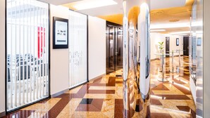 Un couloir d’hôtel moderne avec un comptoir d’enregistrement, un espace de réception et une cloison en verre ornée d’une photographie encadrée.