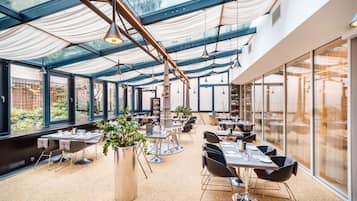 Un vaste espace de restauration intérieur, doté de tables et de chaises, de grandes fenêtres et d’un design de plafond moderne.