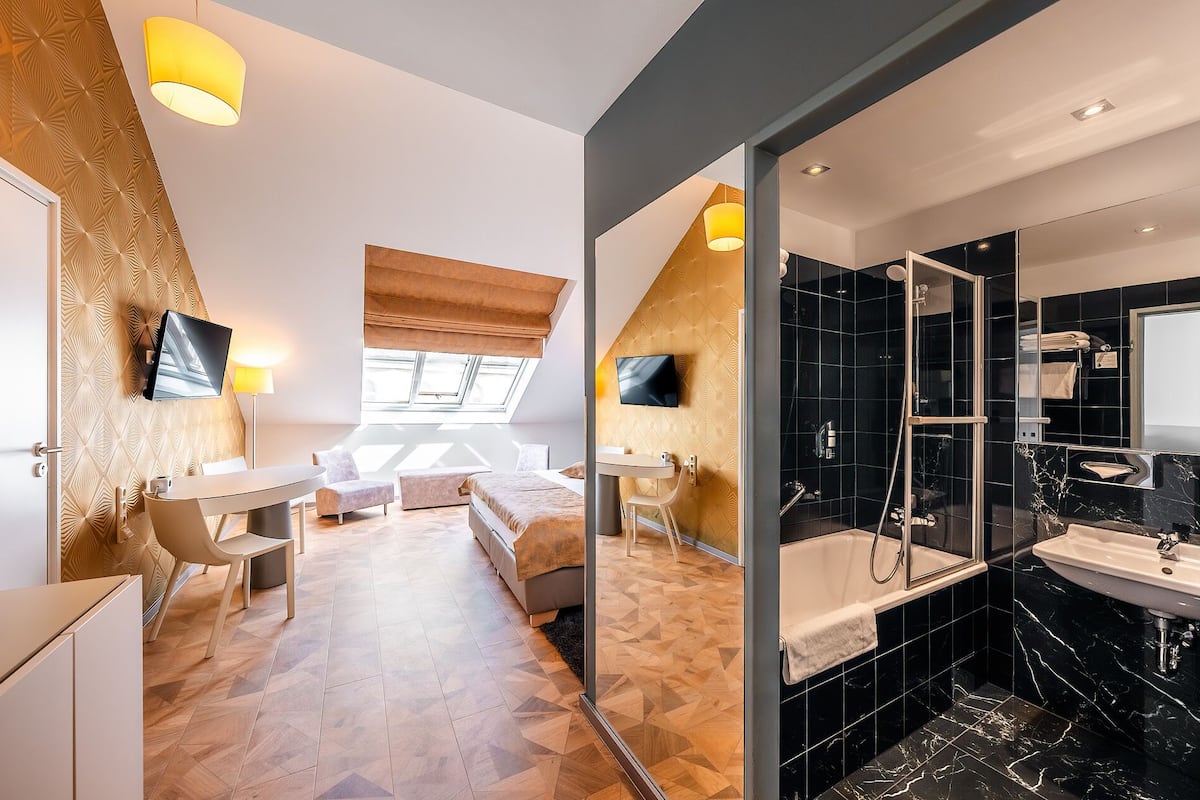 Ein modernes Hotelzimmer mit Hochbett, Schreibtisch, Fernseher, Dusche und einem Badezimmer mit großem Spiegel.