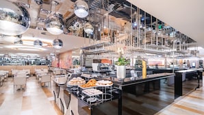 Un restaurant moderne doté d’un plafond haut, de lustres sphériques réfléchissants et d’un espace buffet proposant une variété de plats.