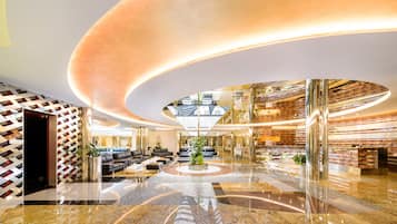 Um hall amplo com área de estar circular central, teto alto com design curvo e um balcão de recepção moderno.