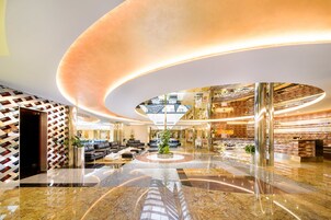 Um hall amplo com área de estar circular central, teto alto com design curvo e um balcão de recepção moderno.