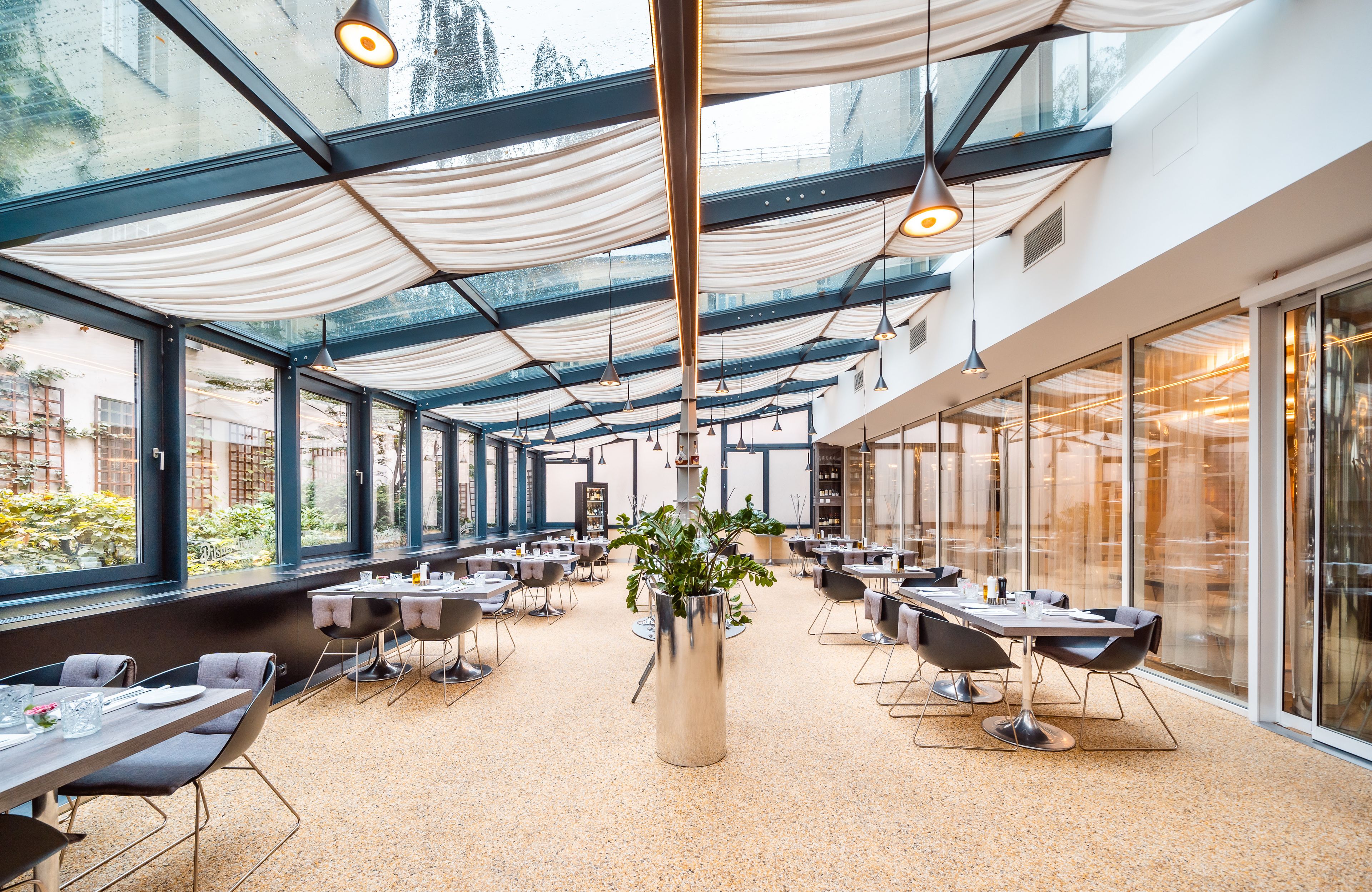 Un vaste espace de restauration intérieur, doté de hauts plafonds, de grandes fenêtres et d’un mobilier moderne.