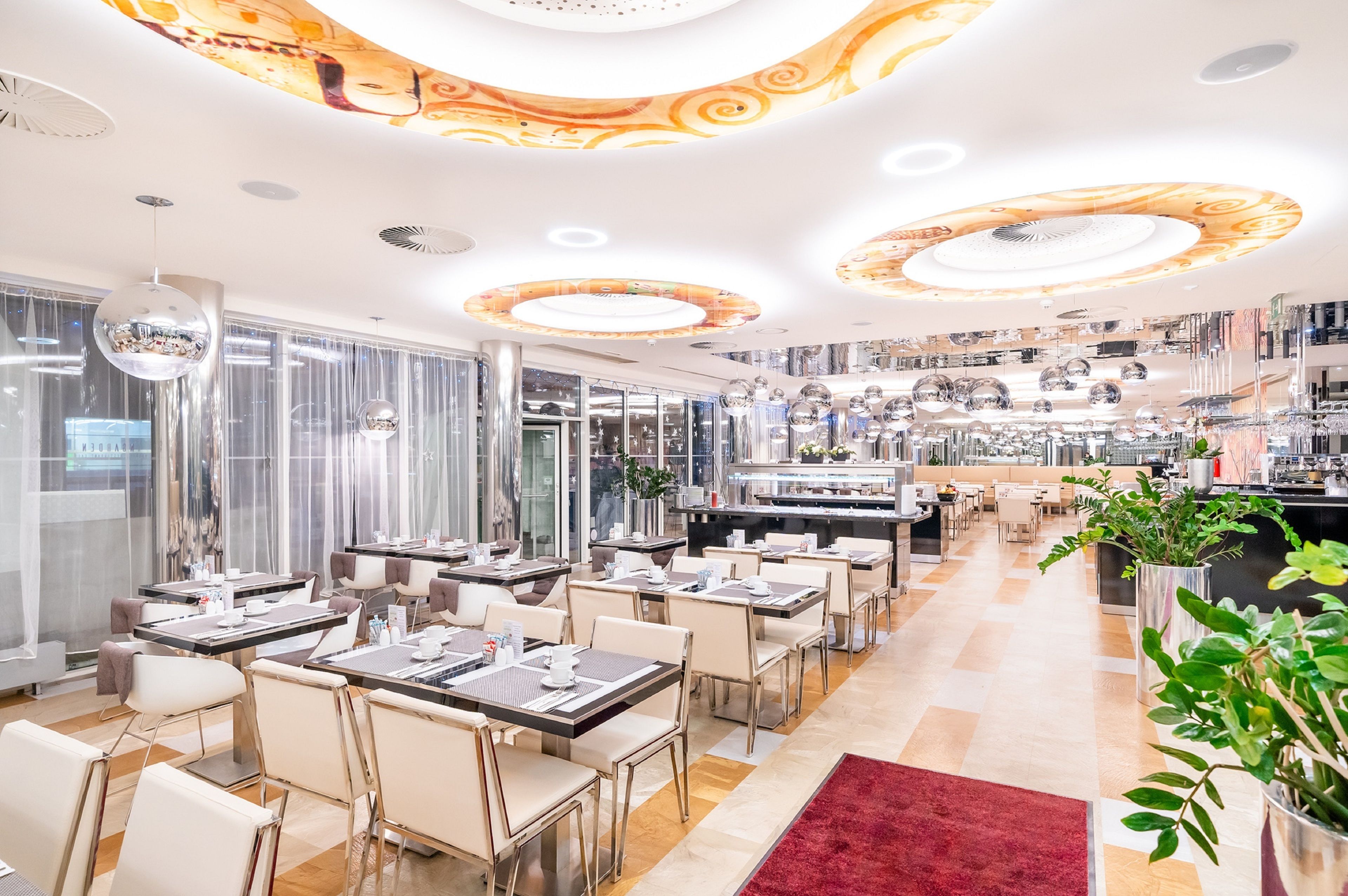 Um restaurante moderno com várias mesas e cadeiras, área de cozinha e luminárias decorativas no teto.
