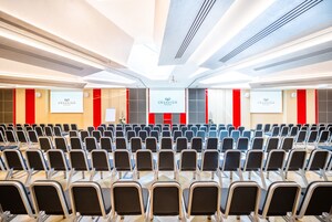 A conference room with rows of chairs, a stage with a podium, and the Grandium Prague logo on the walls.