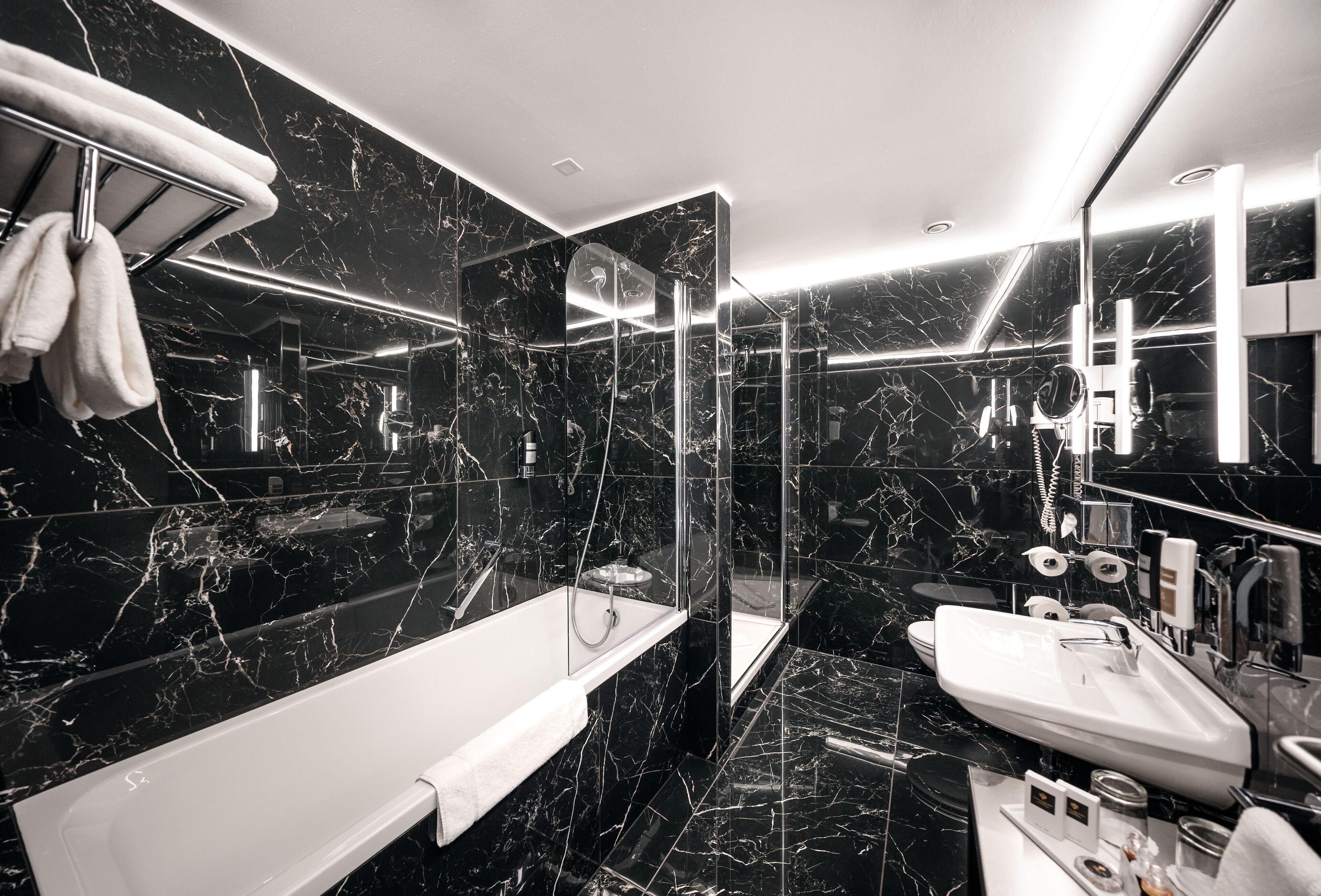 A modern bathroom with a black marble design, a white bathtub, and a separate sink area.